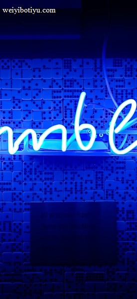 A bright blue neon sign spells out the word 'gambling' in cursive script. The background features a textured wall covered in domino tiles, also illuminated by the blue light, creating a vivid and visually striking scene.